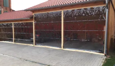 Große transparente PVC-Planen als seitlicher Wetterschutz an einem Carport