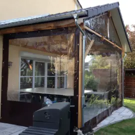 Transparente PVC-Terrassenplane mit dunklem Saum an einer Holzüberdachung